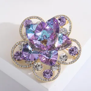 Broche fleur dorée élégante avec cristaux violets et bleus sur un support blanc épuré