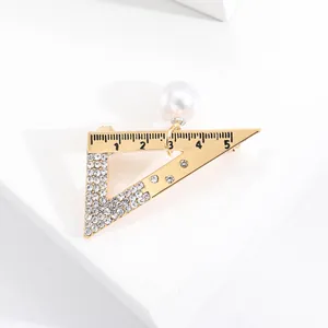 Dettaglio della spilla a triangolo in lega dorata con strass e perla bianca