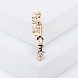 Broche créative en forme de peigne doré avec strass et détails en émail noir sur socle