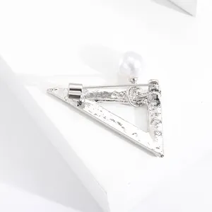 Vista dettagliata della spilla a triangolo argento con trama martellata e grande perla