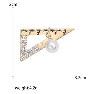 Spilla a righello triangolare dorata con strass bianchi e perla su sfondo bianco puro
