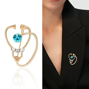 Broche stéthoscope dorée avec cœur en cristal bleu sur fond blanc et sur un costume noir