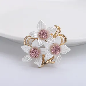 Eleganter Gold-Blumenbrosche mit weißen Blüten und lila Strass auf weißem Porzellan