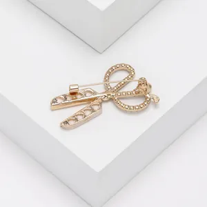 Detalle del broche de tijera dorado con recorte de corazón y cierre de alfiler seguro