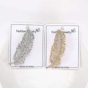 Dettaglio di spille a piuma in oro e argento con cristalli su scheda espositiva