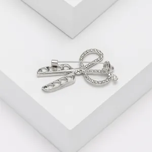 Detalle del broche de tijeras plateadas con pedrería brillante y corazones calados en pedestal