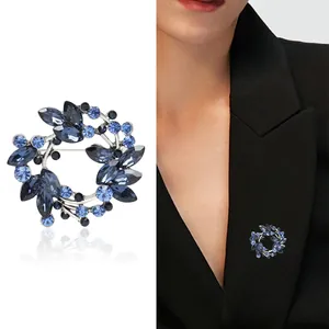 Elegant silver olive branch wreath brooch with blue crystals shown on a model