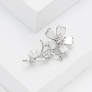 Broche florale argentée avec pétales blancs et perle sur un support géométrique épuré