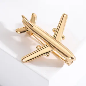Polished golden airplane brooch lapel pin displayed on a minimalist white pedestal stand