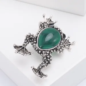 Detailed macro of vintage silver frog brooch featuring a green teardrop gemstone inlay