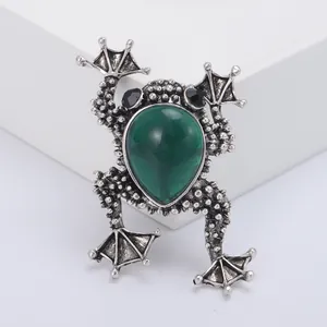 Vintage silver frog brooch with large green teardrop gemstone on a display stand