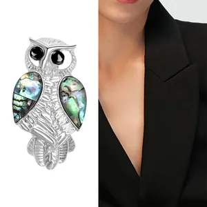 Artistic silver owl brooch featuring abalone shell inlay and black gemstone eyes on suit
