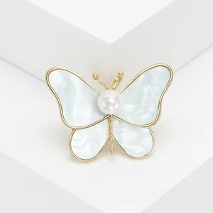 Elegant butterfly brooch with blue shell wings and central pearl on minimalist display