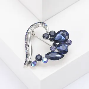 Detail of silver heart brooch with blue and purple crystals on white pedestal
