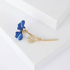 Détail de la broche fleur mate bleue avec tige dorée sur un socle blanc