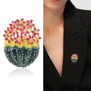 Broche cactus en émail avec fleurs rouges portée sur le revers d'un blazer noir