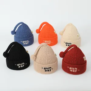 Mise à plat de bonnets en tricot avec lettrage Sunday et pompons de couleurs variées