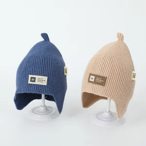 Close-up of children's knit beanies with ear flaps, pointy tops and letter patches