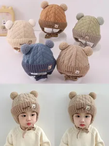 Detailansicht der gesteppten Baby-Ohrenklappenmützen mit Bären-Patch und doppelten Pompons
