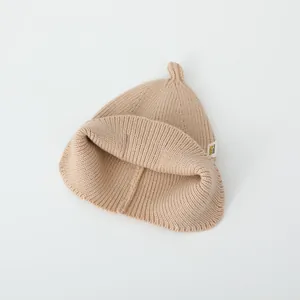 Minimalist beige knitted baby beanie with ear protection and pointed top design