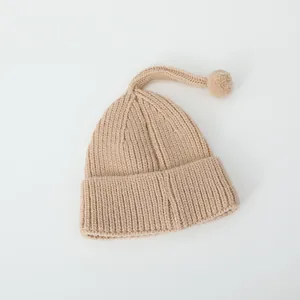 Détail du tricot d'un bonnet d'hiver beige pour bébé avec pompon et queue souple
