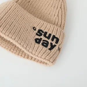 Gros plan du bonnet en tricot beige pour bébé avec broderie Sunday et texture