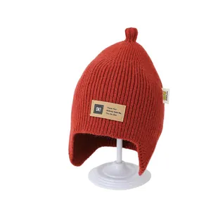 Winter knitted baby beanie with earflaps and letter patch in rust red wool material