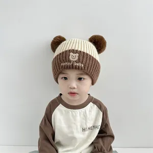 Detail der Baby-Strickmütze für den Winter mit Pompons und Bären-Stickerei