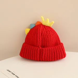 Detail of red knit kids hat featuring cartoon dinosaur fins and a yellow crown decor