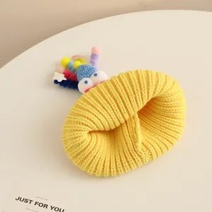 Detail view of yellow knit baby hat with colorful pom-poms and funny 3D eyes decoration