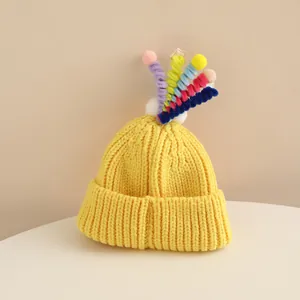 Detail of yellow knit child hat with colorful spiral pom-poms and rolled cuff texture