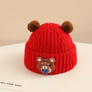Dettaglio cappello in maglia rossa per neonati con orecchie da orso e badge in silicone