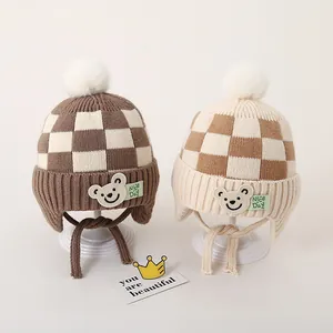 Winter gebreide babymuts met beer-patch en pompon in stijlvol geruit patroon