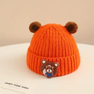 Dettaglio cappello neonato in maglia arancione con orecchie d'orso e stemma cartoon