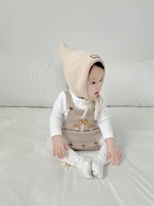 Baby wearing a beige knitted pointed hat and romper set with mushroom embroidery detail