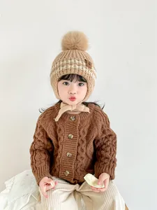 Detail view of children's thick knit cardigan with wooden buttons and pom pom earflap hat