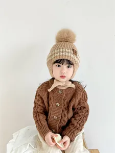 Detail of children's knit hat with faux fur pompom, ear flaps, and braided knit cardigan