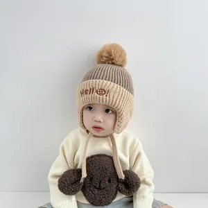 Detail of baby winter knit hat with Hello smiley embroidery and large plush pom-poms