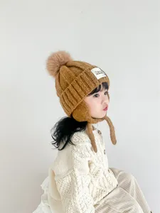 Detailed view of kids winter knit hat featuring earflaps and a plush brown faux fur pom