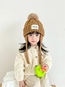Close-up of children's knit trapper hat with fluffy pompom and logo patch detail