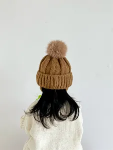Detail of caramel knit kids hat with large fluffy faux fur pompom and ribbed texture