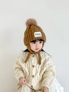 Detailed close-up of brown knit baby earflap hat with fluffy pompom and label