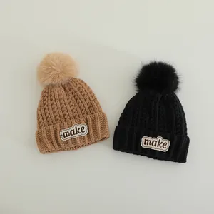 Close-up of winter knit beanies with fluffy pom poms and make letter patch detailing