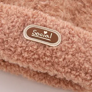 Dettaglio della texture in peluche con toppa in pelle 'Social' su berretto invernale rosa