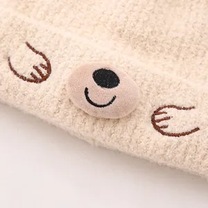 Détail du bonnet en polaire beige avec broderie ours et texture douce et moelleuse