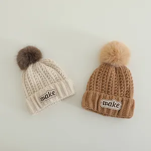 Winter kids knit hats with fluffy pom-poms and MAKE letter embroidery in beige and camel