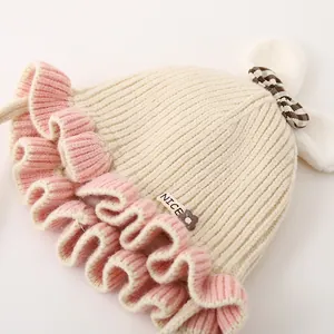 Détail d'un bonnet tricoté pour bébé avec texture côtelée beige, volants roses et oreilles de lapin