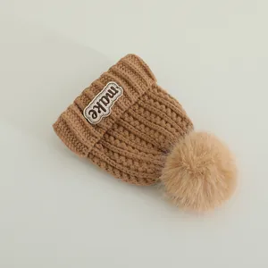 Close-up of winter knit hat with MAKE embroidery label and fluffy faux fur pom-pom