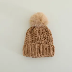 Detail of winter knit hat featuring thick ribbed texture and fluffy brown pom-pom
