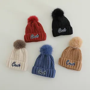 Detail of five assorted winter knit hats with fluffy faux fur pom-poms and Crush patches